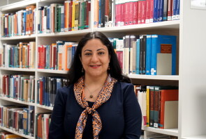 Tutkijatohtori Mehrnoosh Farzamfar oikeustieteellisen tiedekunnan kirjastohyllyjä taustallaan