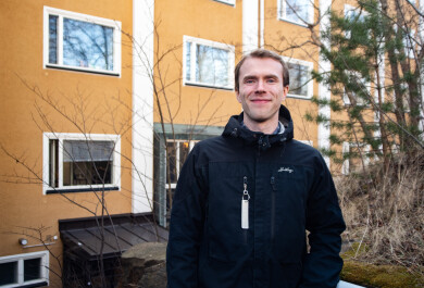 Tutkija kuvattuna ulkona keltaisen kerrostalon edustalla