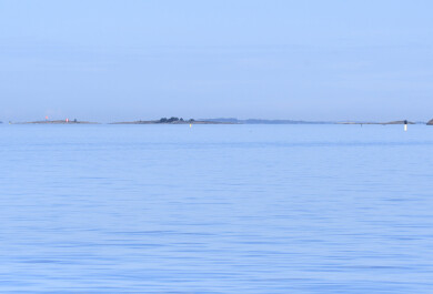 Utuinen merimaisema, jossa horisontissa näkyy saari ja merimerkkejä