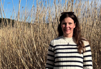 Nainen seisoo kaislikon edessä ja katsoo kameraan.