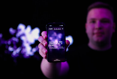 Henkilö pitelee älypuhelinta, jonka näytölle on kirjoitettu tekstiä. Taustalla on violettia valoa.