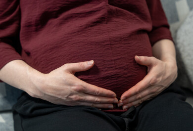 Äiti pitää käsiä raskausvatsansa päällä.