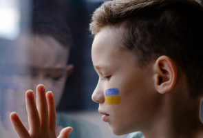 Lapsi ikkunalla, kasvoihin maalattu Ukrainan lippu.