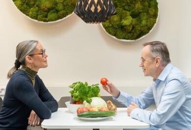 Kati Hanhineva ja Jorma Toppari istuvat vastakkain pöydän ääressä. Pöydällä on tuoreita kasviksia.