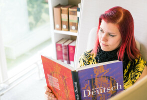 Kirjastossa oleva henkilö lukee saksan kielen oppikirjaa.