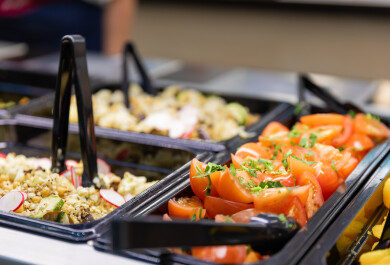 lähikuvassa itsepalveluravintolan linjaston salaattikippoja, joissa tomaattilohkoja ja salaatteja sekä ottimia