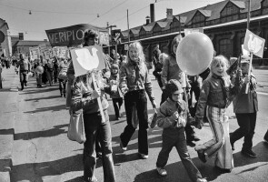 Vappumarssijoita Hämeentiellä. Edessä lapset kantavat kylttejä, joissa rauhankyyhkyn kuva. Keskellä edessä lapsi ilmapallon kanssa. Takana kannetaan banderollia, jossa teksti: Meripioneerit.