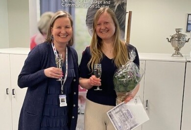 Kaksi henkilöä katsoo kameraan ja hymyilee, käsissään kuohuviinilasit ja toisella myös kukkakimppu ja diplomi.