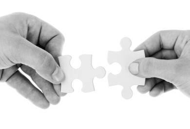 Kaksi kättä pitelemässä palapelin paloja lähekkäin.