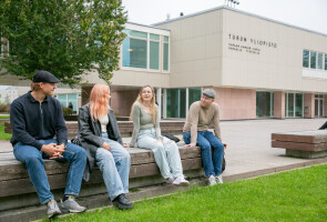 Opiskelijoita Turun yliopiston päärakennuksen edessä penkillä.