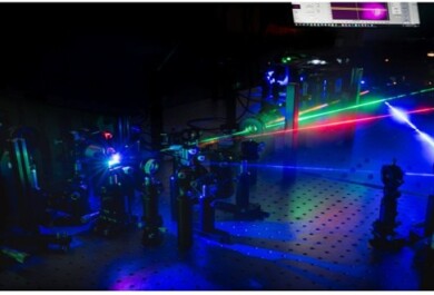 Dark laboratory setting where four different coloured lasers point to different directions, emanating a blue glow.