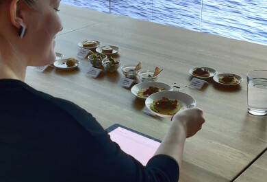 Nainen tarkastelee pöydällä olevia pieniä kala-annoksia. Seinälle on heijastettu merimaisema.