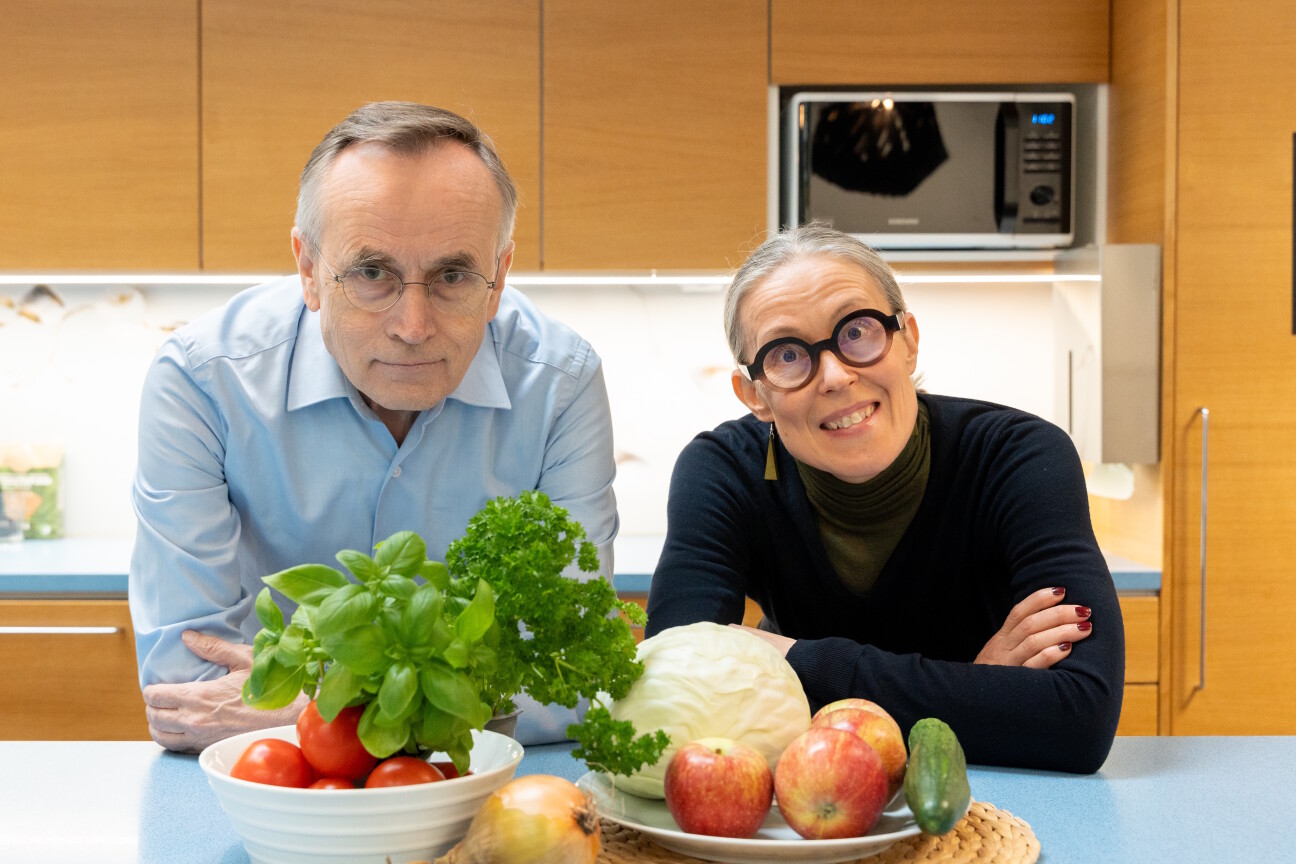 Kati Hanhineva ja Jorma Toppari nojaavat pöytään keittiössä, pöydällä vihanneksia.