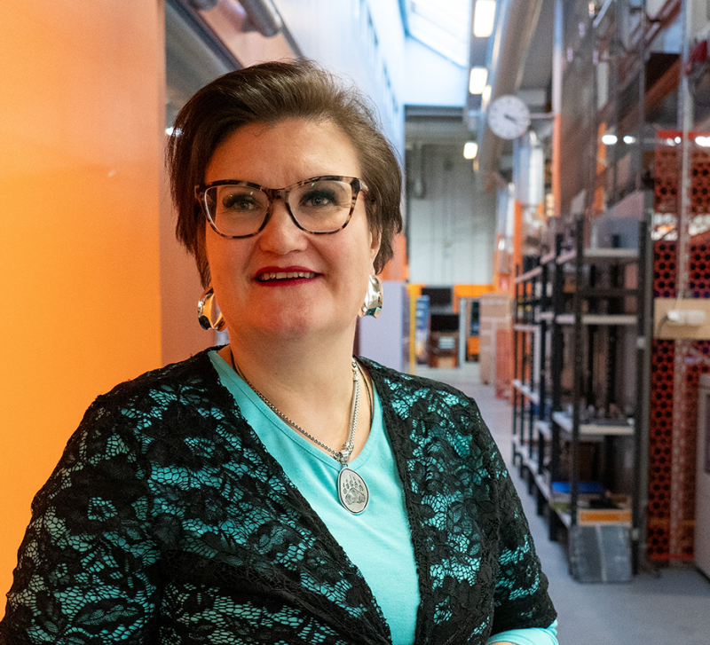 Heidi Piili konetekniikan hallissa pitkällä käytävällä, kasoo kohti kameraa, vieressä oranssi seinä