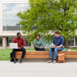 Ihmisiä istumassa ulkona penkillä, taustalla puu ja yliopiston Feeniks-kirjasto.