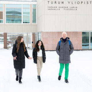Three doctoral researchers walking outside the University's main building in winter