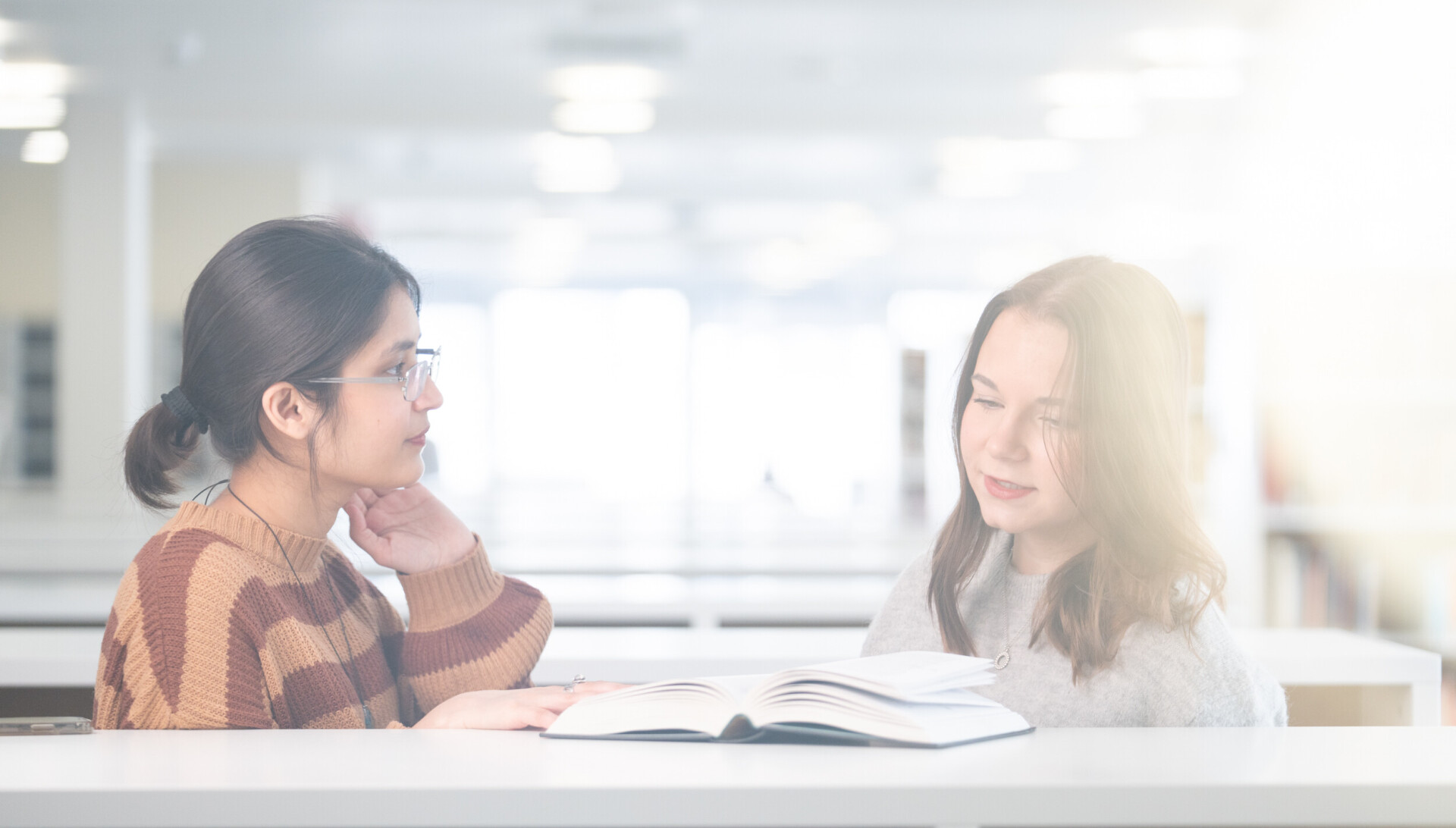 Two people examining a book in the library