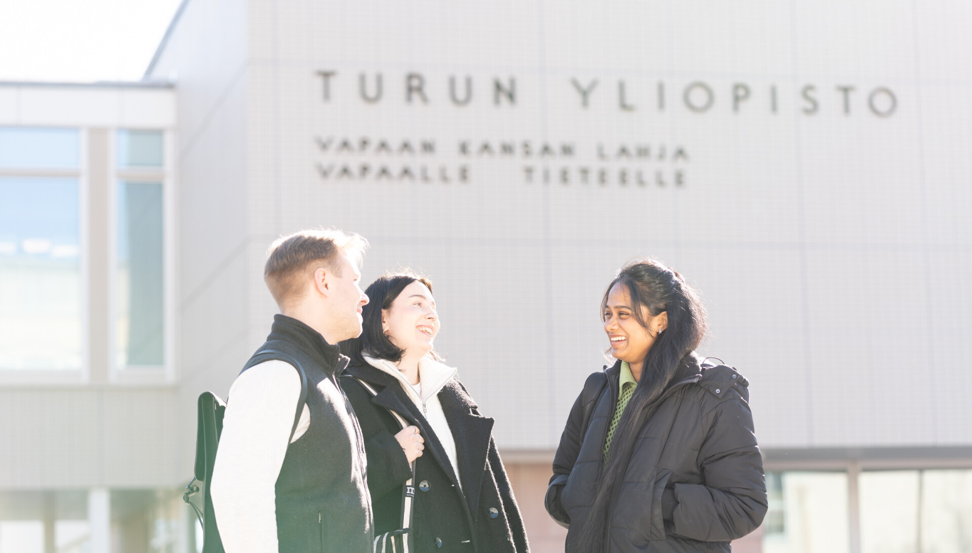 Kolme henkilöä juttelemassa iloisesti Turun yliopiston päärakennuksen edessä